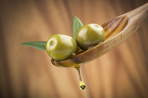 Two olives and leaves with drop oil on wood spoon